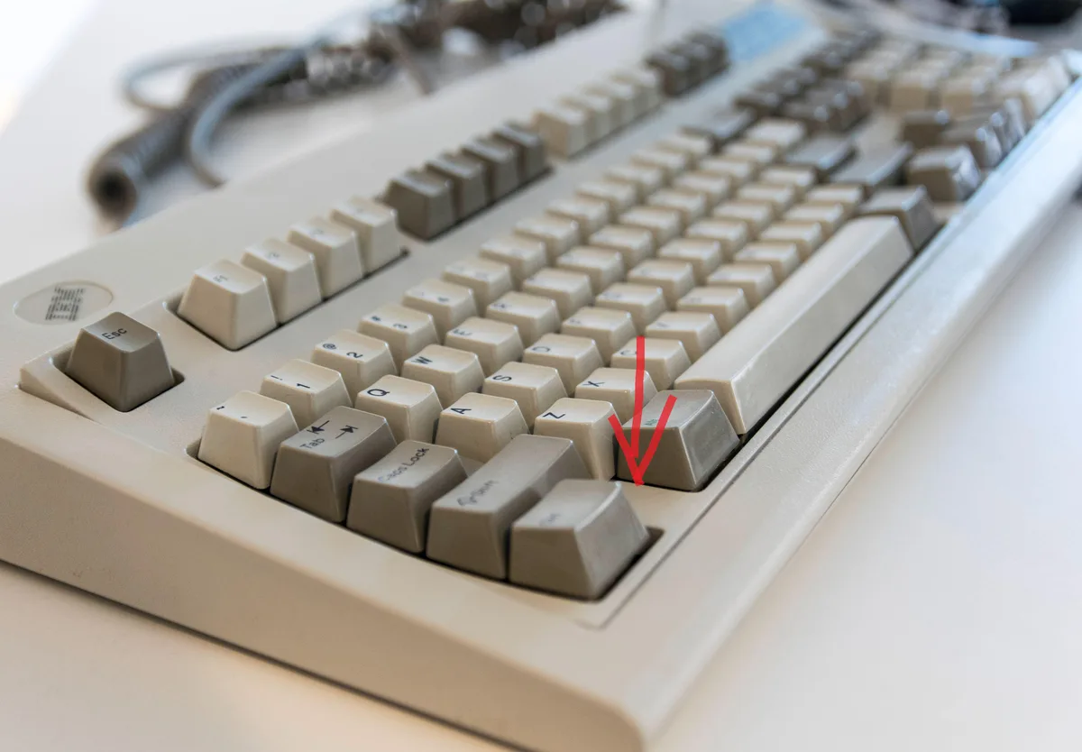 A close-up photo of a beige ibm keyboard with a red arrow drawn over it, pointing directly at the 'z' key. The keyboard has…