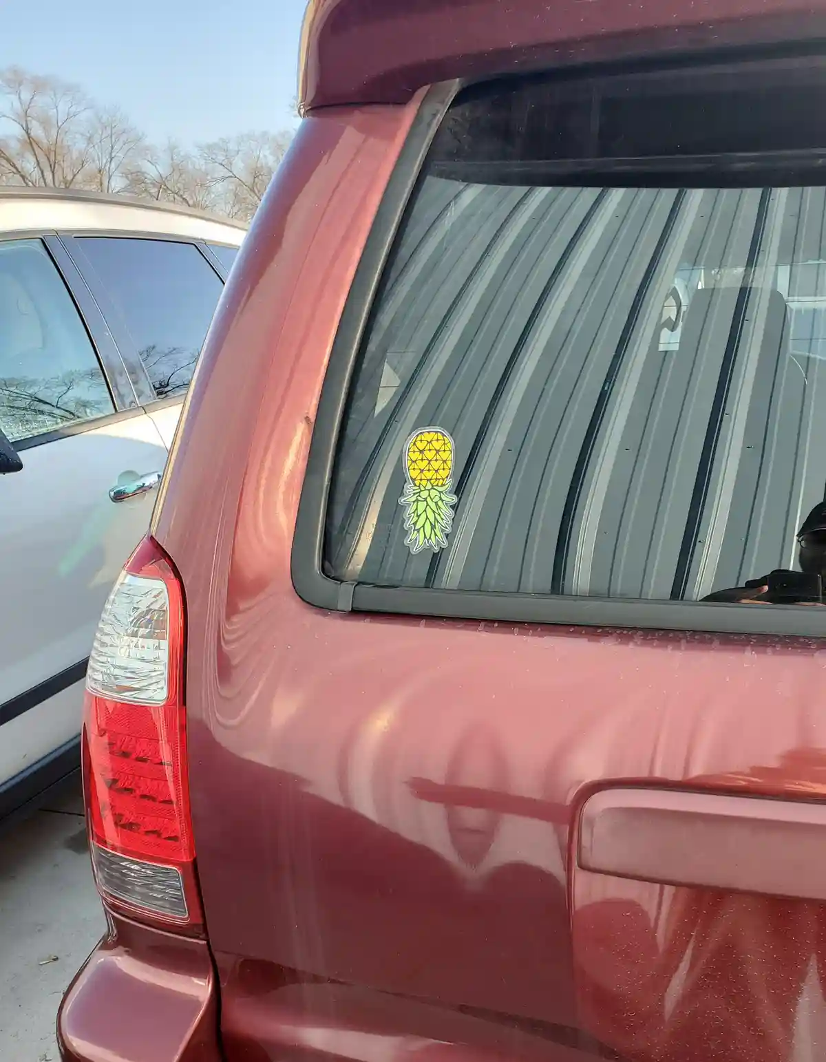 A close-up photo shows the rear of a maroon Toyota vehicle parked next to a white car, with a yellow pineapple-shaped…