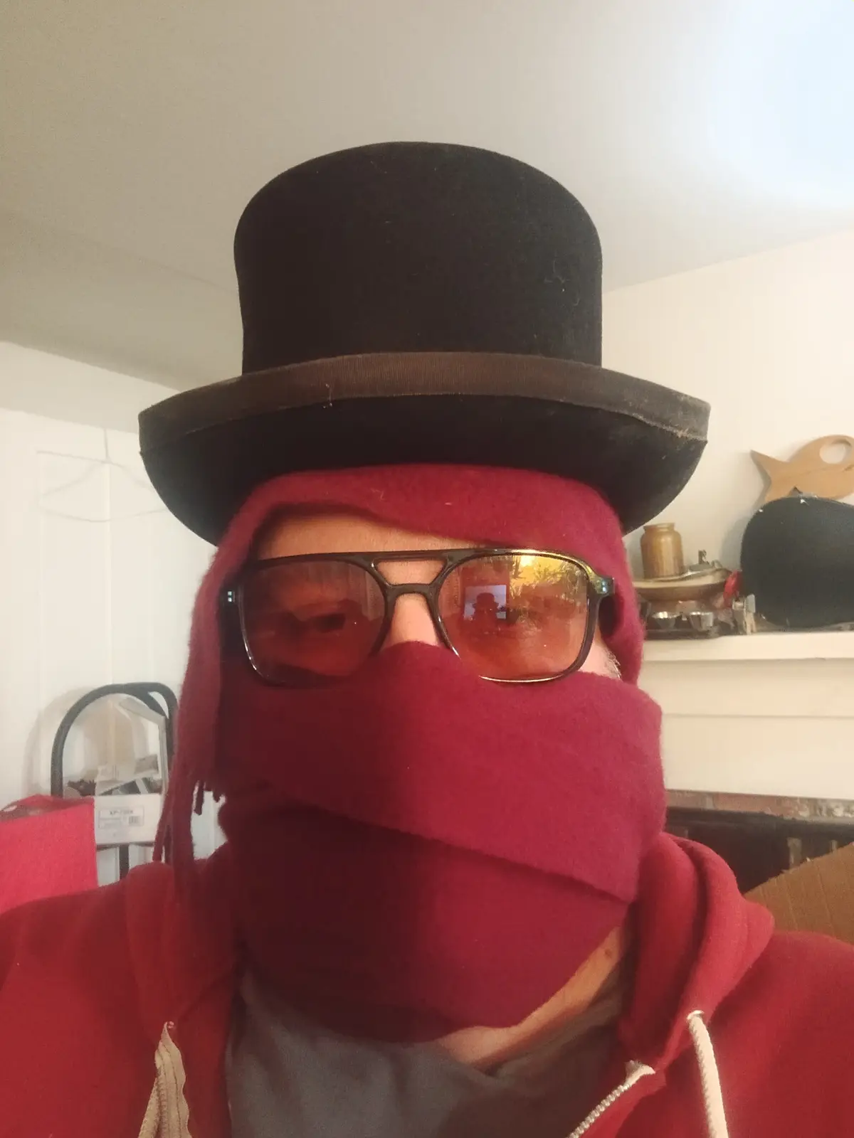 A person wearing a black top hat, a red fleece face covering that obscures their mouth and nose, and large reflective…