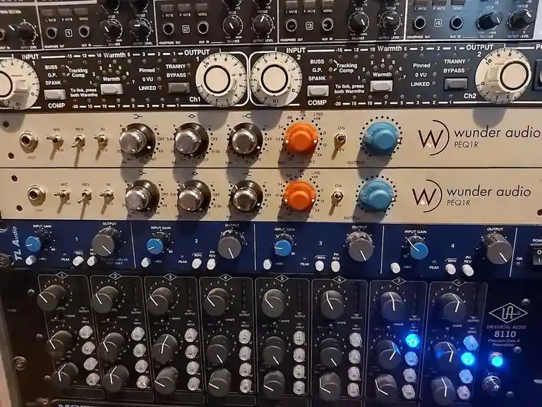 A close-up photo of a rack of professional audio equipment, including two Wunder Audio PEQ1R units and a Universal Audio…