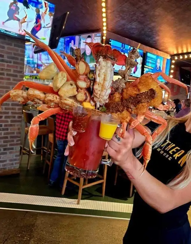 a person in a bar holds a massive, elaborate seafood platter constructed to look like a giant crab claw, complete with crab…
