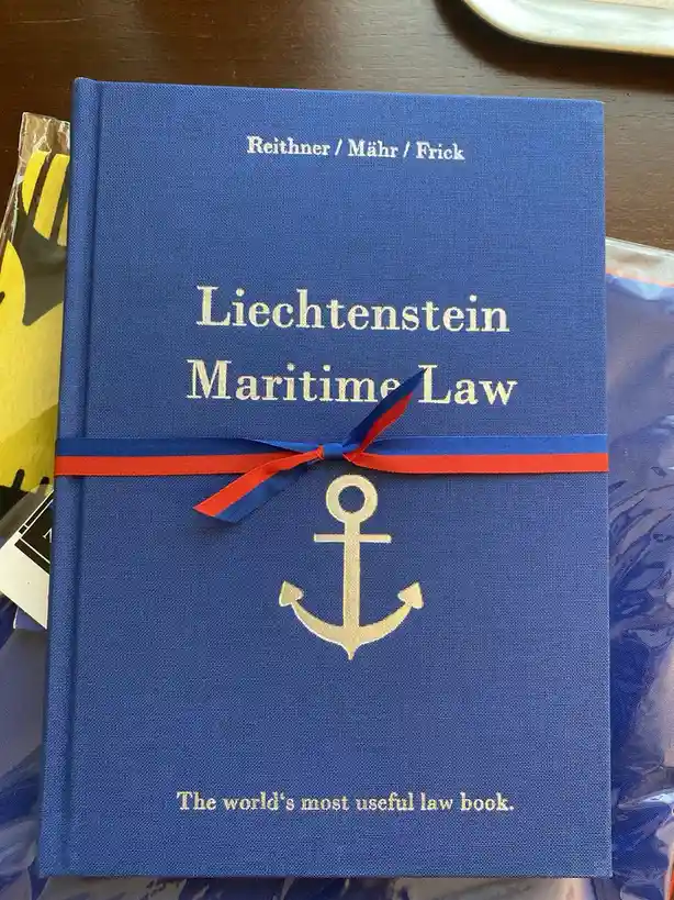 A blue cloth-bound law book titled 'Liechtenstein Maritime Law' by Reithner / Mähr / Frick, featuring a gold anchor emblem…