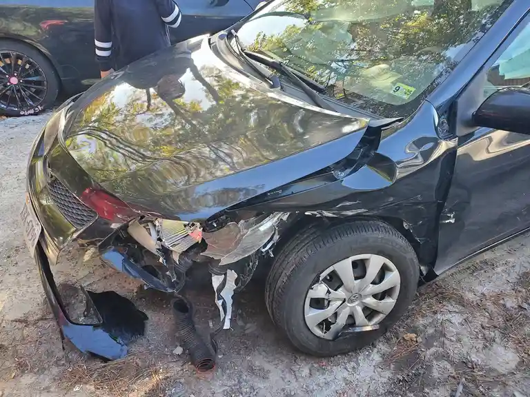 A black car with severe front-end damage, including a crumpled hood, broken bumper, and exposed internal components. A…
