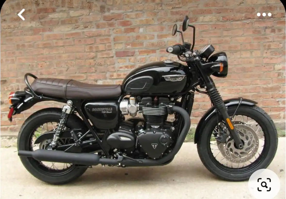A black Triumph Bonneville 750 Black motorcycle is parked in front of a brick wall, showing its full side profile with…