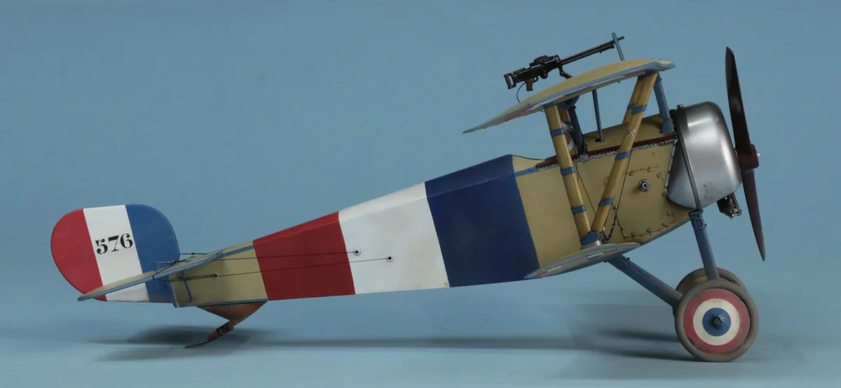 A detailed model of a vintage French biplane, painted with red, white, and blue stripes and the number 576 on its tail, is…