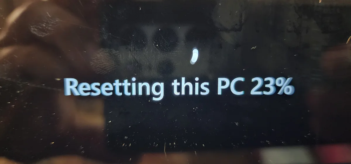 A close-up of a computer screen showing the text 'Resetting this PC 23%' in white font against a dark background, with a…