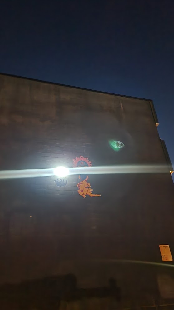 A nighttime photo of a brick wall with a bright light source causing a lens flare. On the wall are three orange…