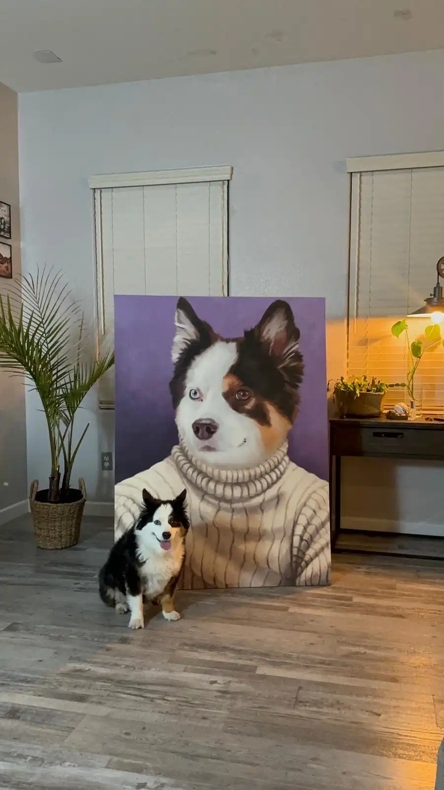 A small black and white dog sits on a wooden floor in front of a large, realistic portrait painting of itself wearing a…
