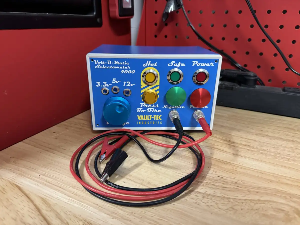 A blue, custom-built electronic device labeled 'Volt-O-Matic Selectometer 9000' by 'VAULT-TEC INDUSTRIES' sits on a wooden…