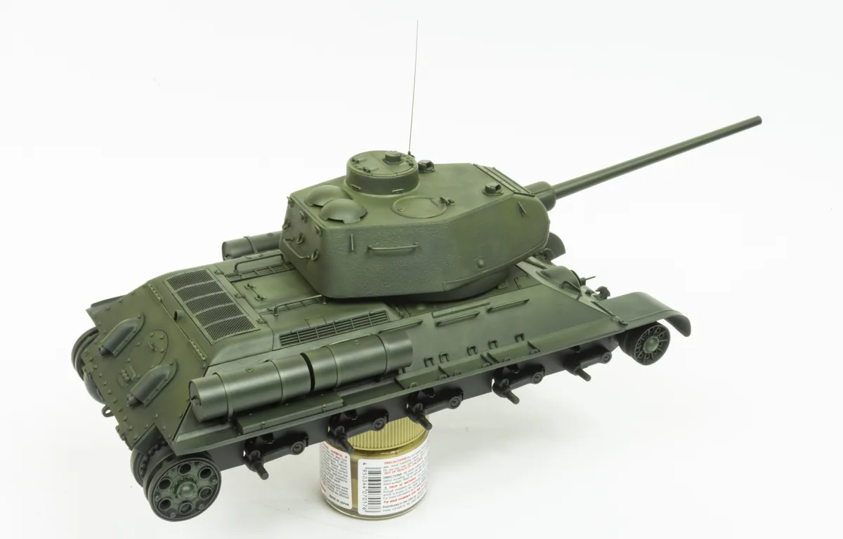 A green model tank is shown balanced precariously on top of a small paint can, with its undercarriage resting on the can's…