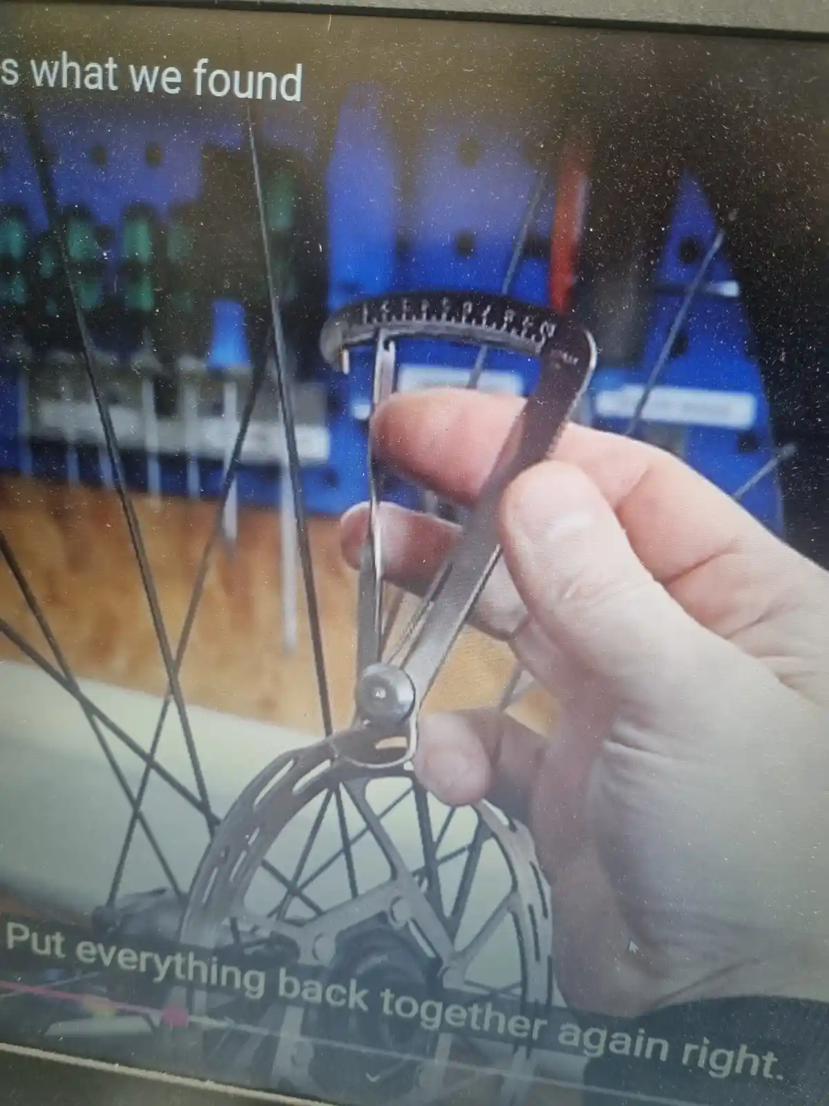 A hand holds a bicycle wheel truing stand against a bike wheel, with overlaid text reading 'This is what we found' at the…