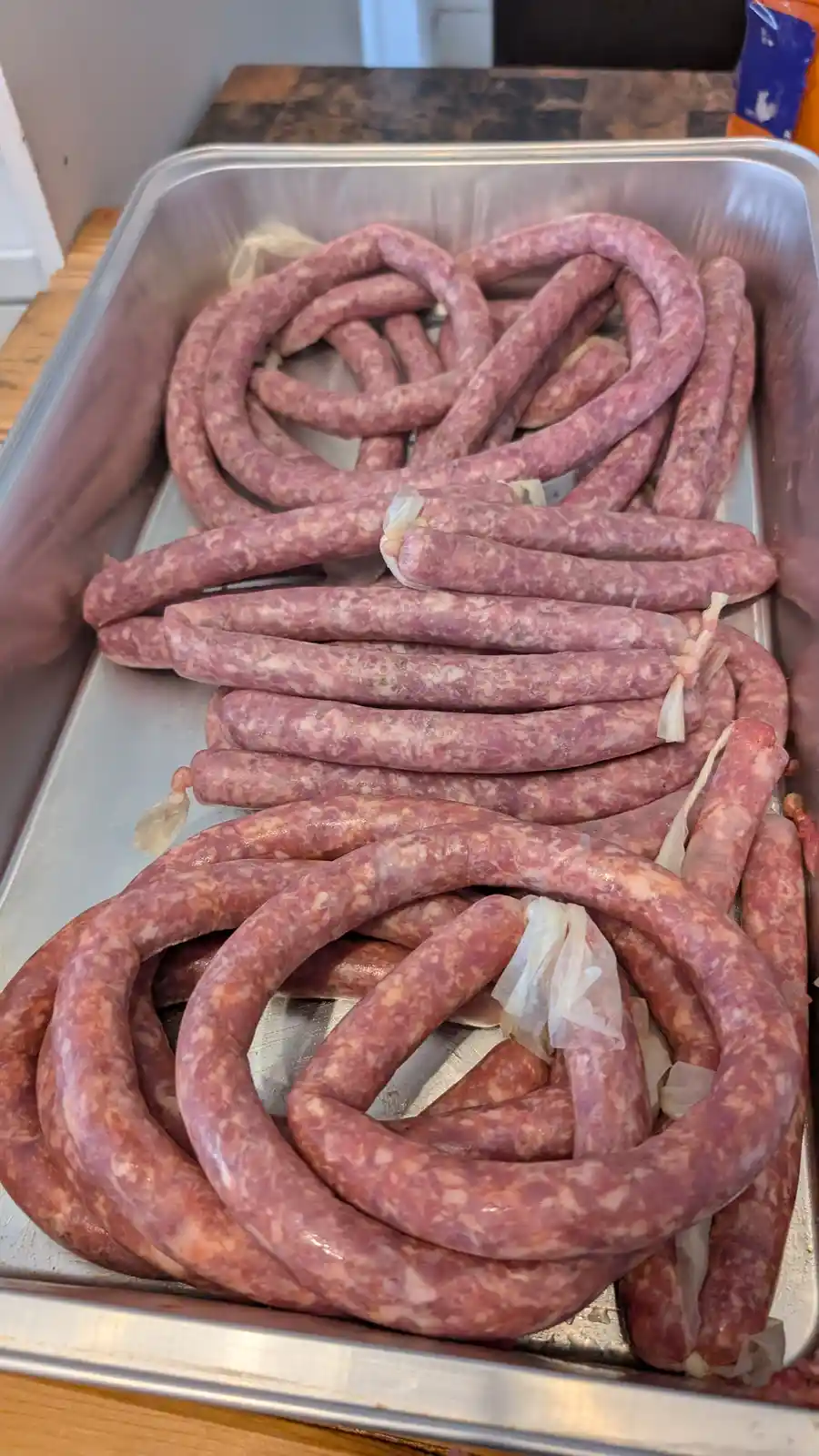 A metal tray holds numerous raw sausages, some coiled into large, distinct heart shapes, while others are laid out in…