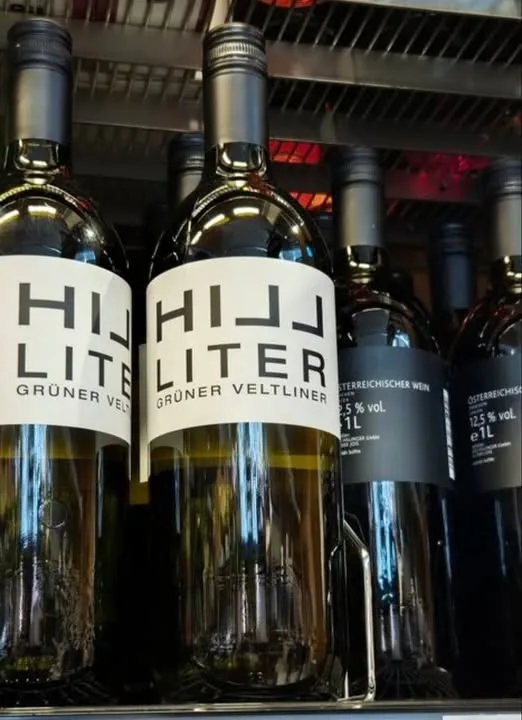 Several wine bottles are lined up on a store shelf, with two prominently featured bottles having labels that read 'HIJJ…