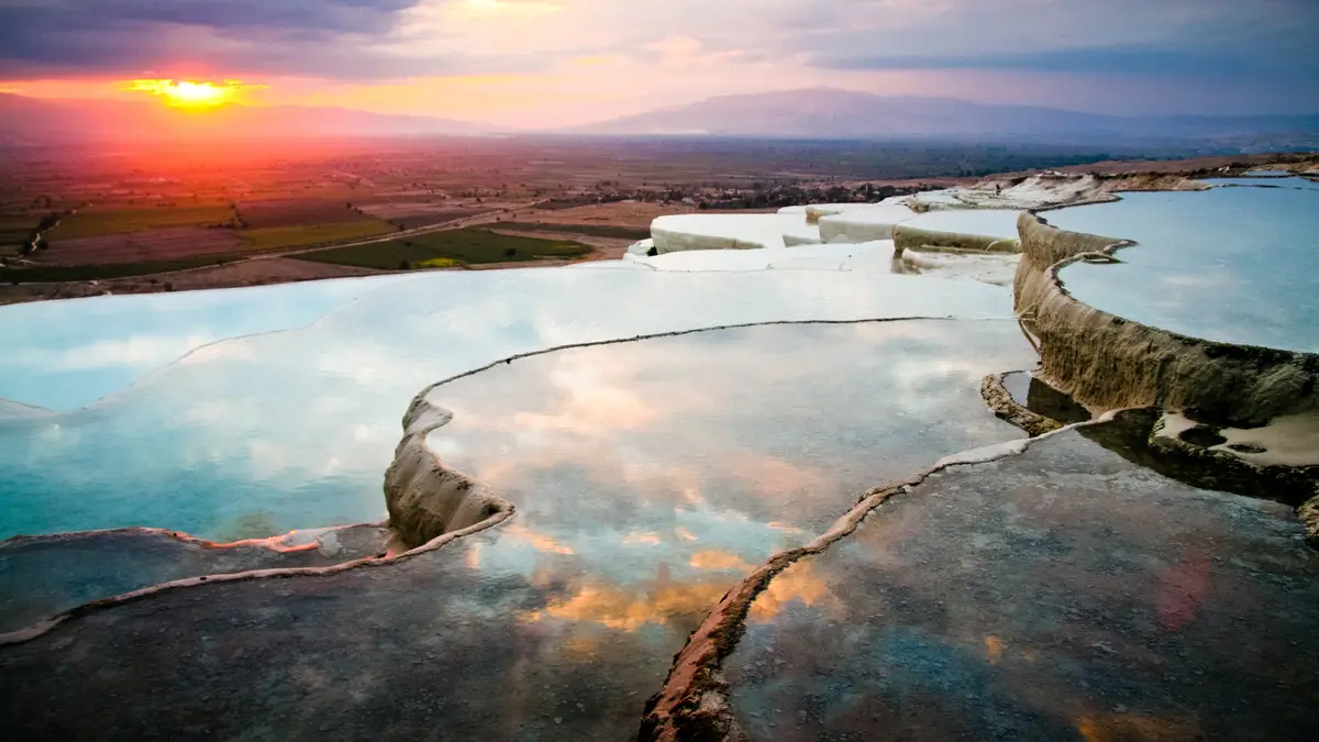Pamukkale's cloud-white travertine terraces glow bright at daybreak, showcasing the Turkish landmark's golden hues. By…