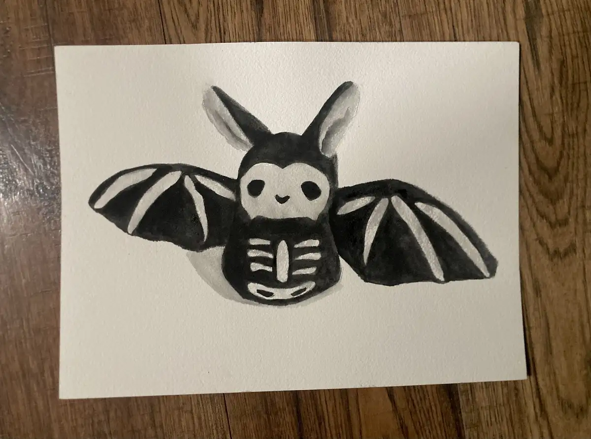 A hand-drawn black-and-white illustration on white paper shows a cute, cartoonish bat with large ears, a smiling face, and a…