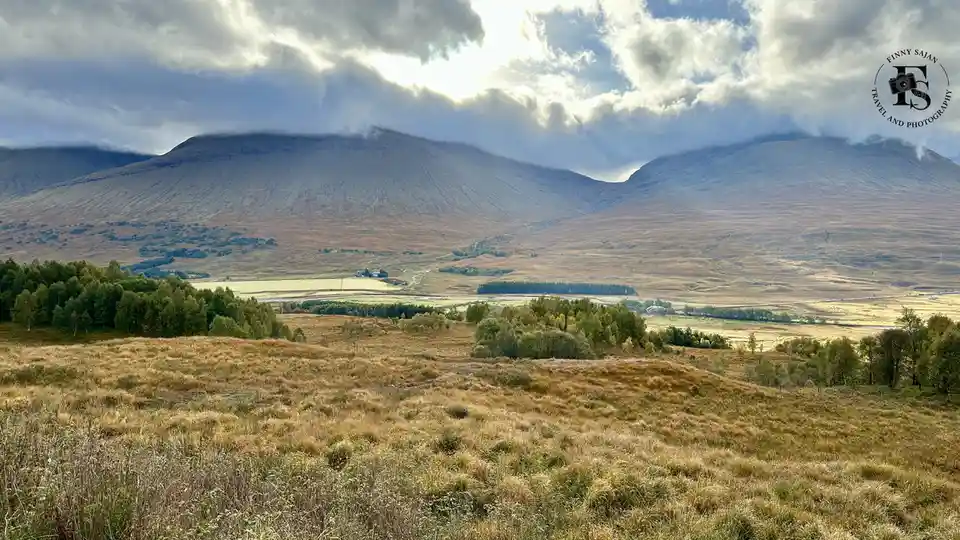 A scenic landscape photo shows rolling hills covered in dry, golden-brown grass with scattered green trees in the…
