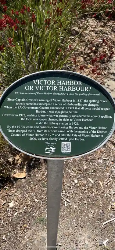 A green, oval-shaped historical information sign in Victor Harbor, Australia, explains the town's name spelling history…