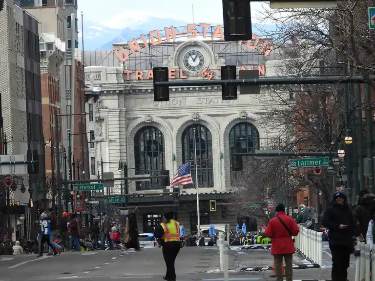 A street-level photo of Denver's Union Station, a grand white-beige building with large arched windows and a prominent…