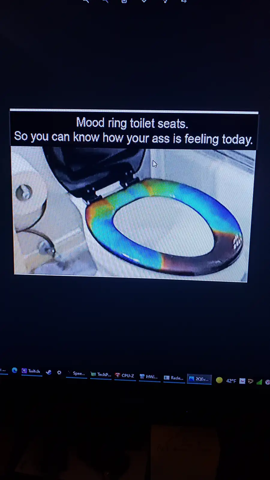 The image shows a toilet seat with a rainbow-colored mood ring around its edge, displayed on a computer screen. The overlaid…