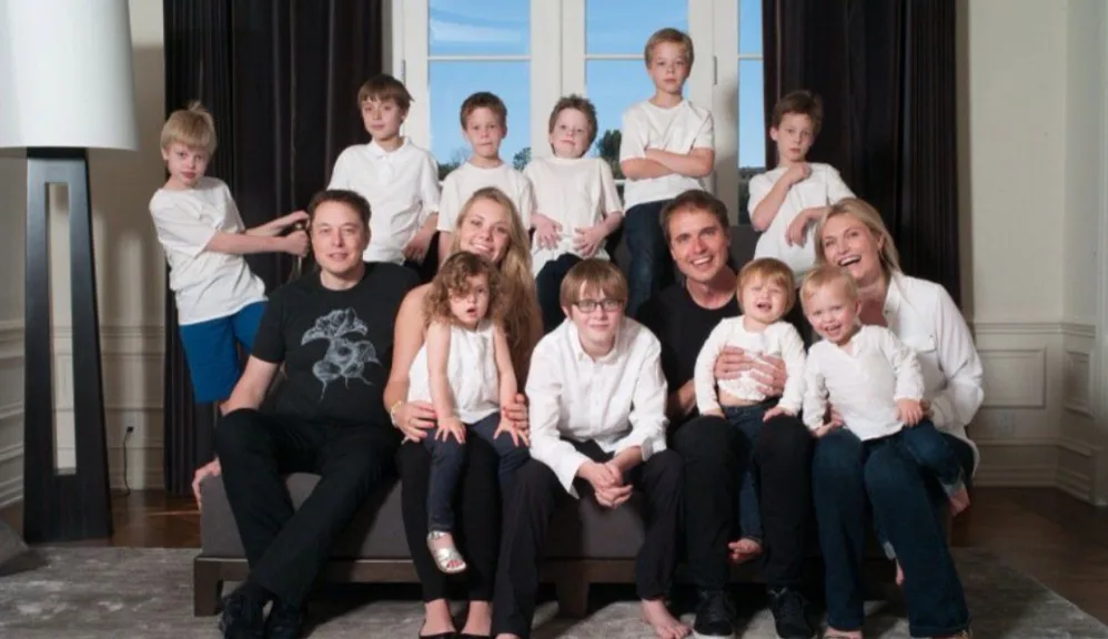 A family photo shows Elon Musk and Elton John seated on a couch with numerous children around them, all dressed in white…