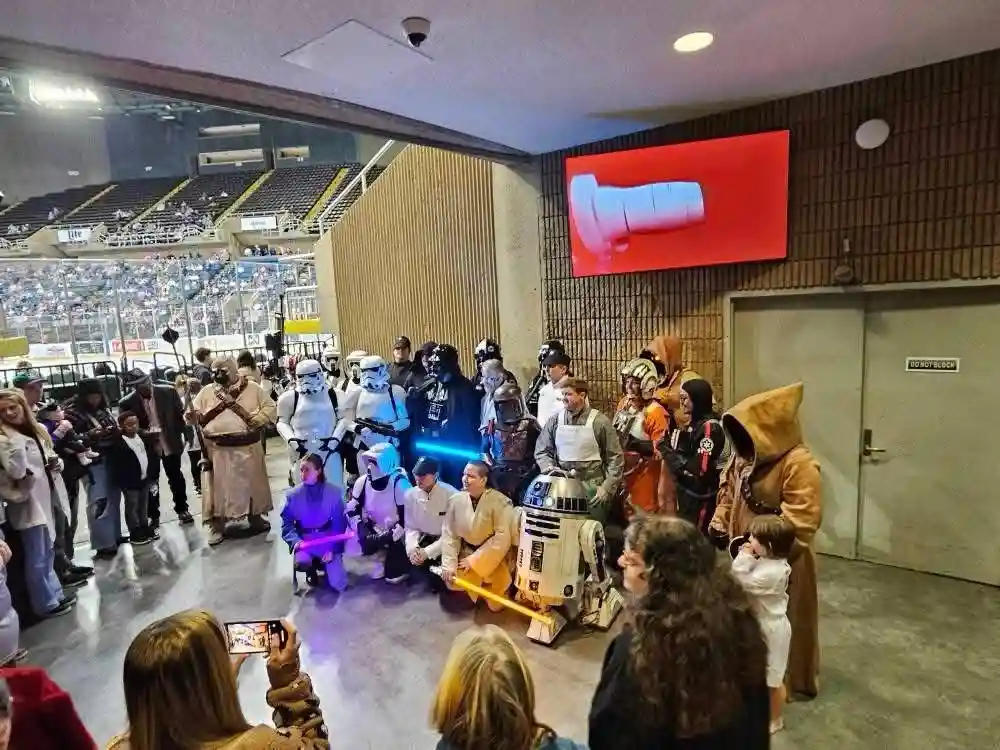 A group of people dressed as Star Wars characters, including Stormtroopers, Darth Vader, R2-D2, and Jedi, pose for a photo…