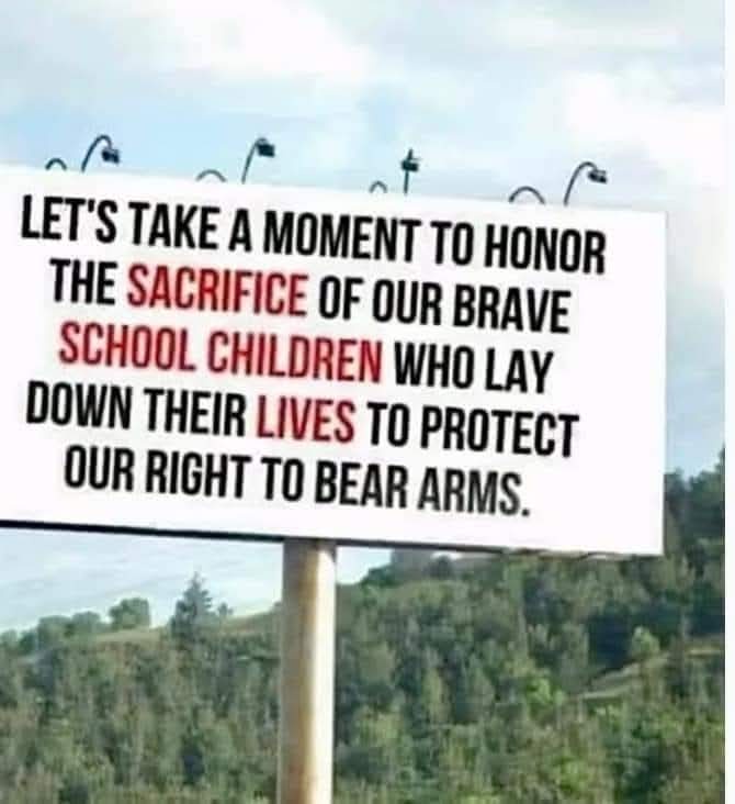 A large white roadside billboard with black and red text reads: 'LET'S TAKE A MOMENT TO HONOR THE SACRIFICE OF OUR BRAVE…