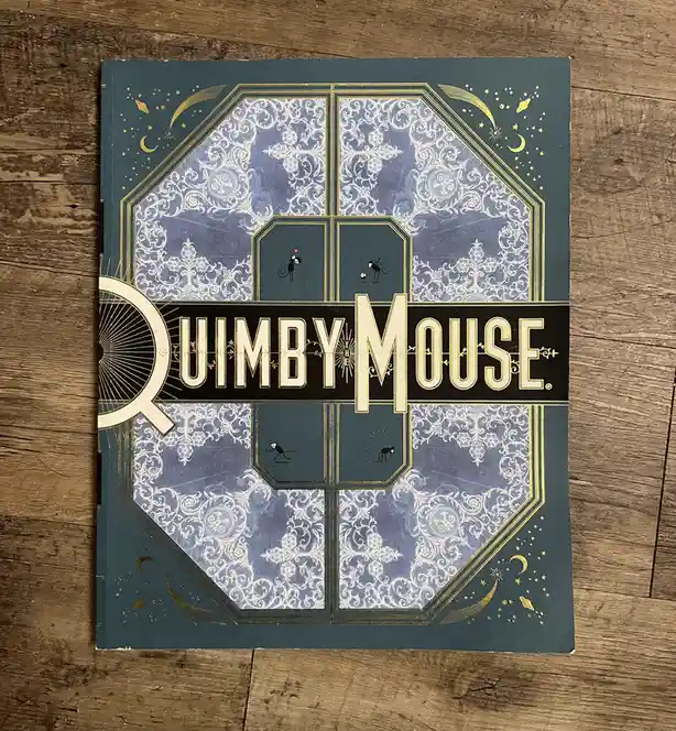 A book cover for 'Quimby Mouse' featuring ornate blue and gold designs with small mouse illustrations in panels, resting on…