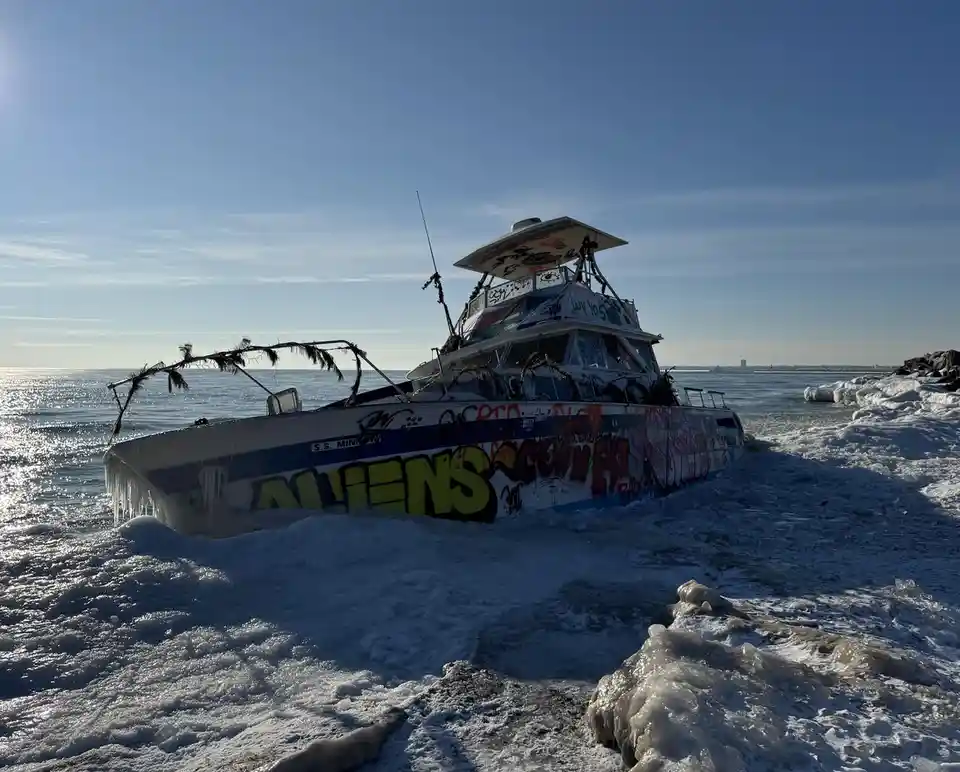 A boat named 'S.S. MINNOW' is stuck in icy water, covered in graffiti including the word 'ALIENS' in large yellow letters…
