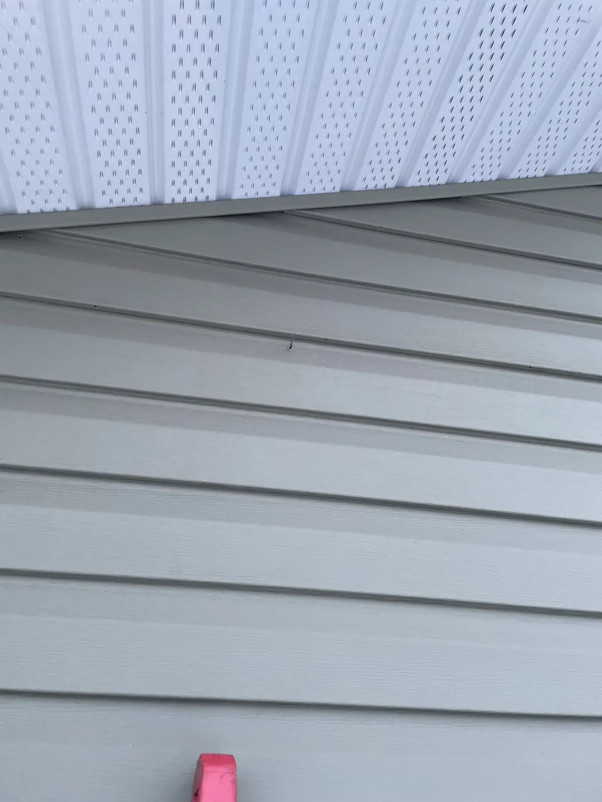 A close-up photo shows the corner where a light gray horizontal siding wall meets a white perforated metal roof. A single…
