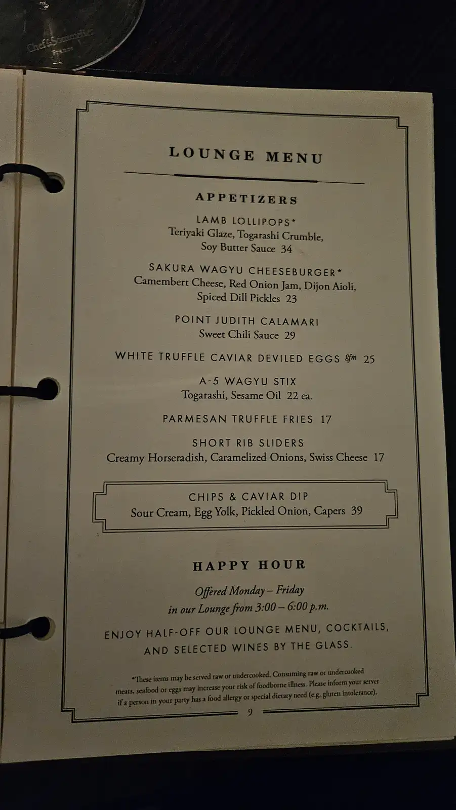 A close-up photo of a restaurant's lounge menu page listing expensive appetizers like 'Lamb Lollipops' and 'Sakura Wagyu…