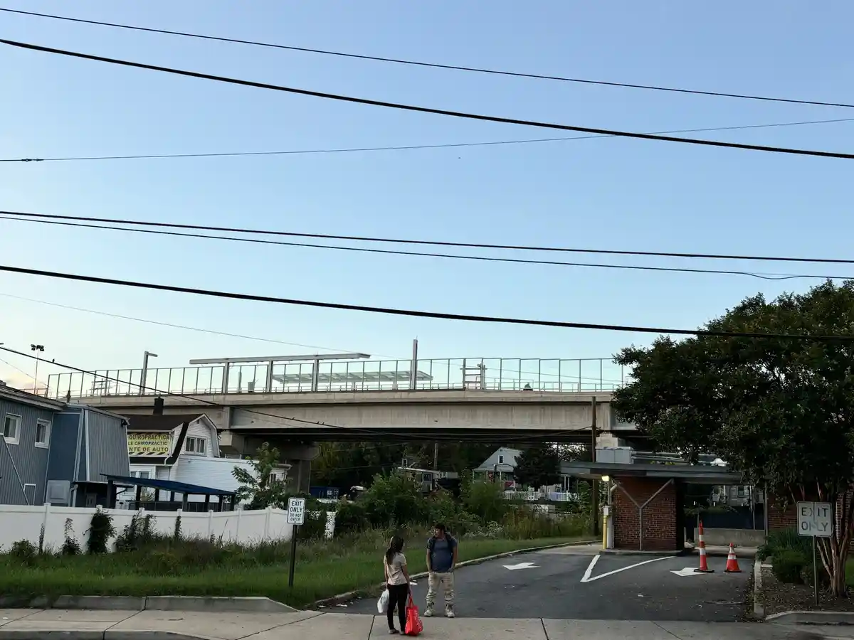 Two people stand at the bottom of a road under a bridge, facing each other. Two white "EXIT ONLY" signs are visible on…