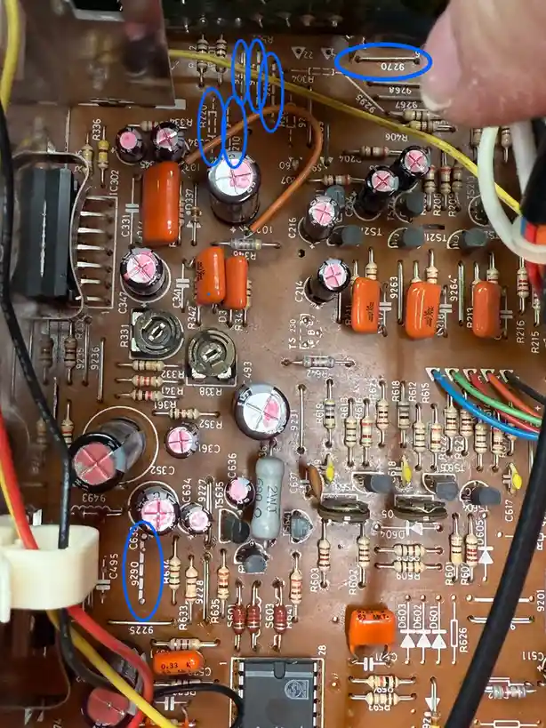 A close-up photo of an electronic circuit board with various resistors, capacitors, and wires. Three small metal strips…