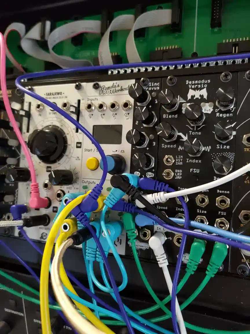 A close-up photo of a densely wired modular synthesizer setup with colorful patch cables tangled around knobs and jacks on…