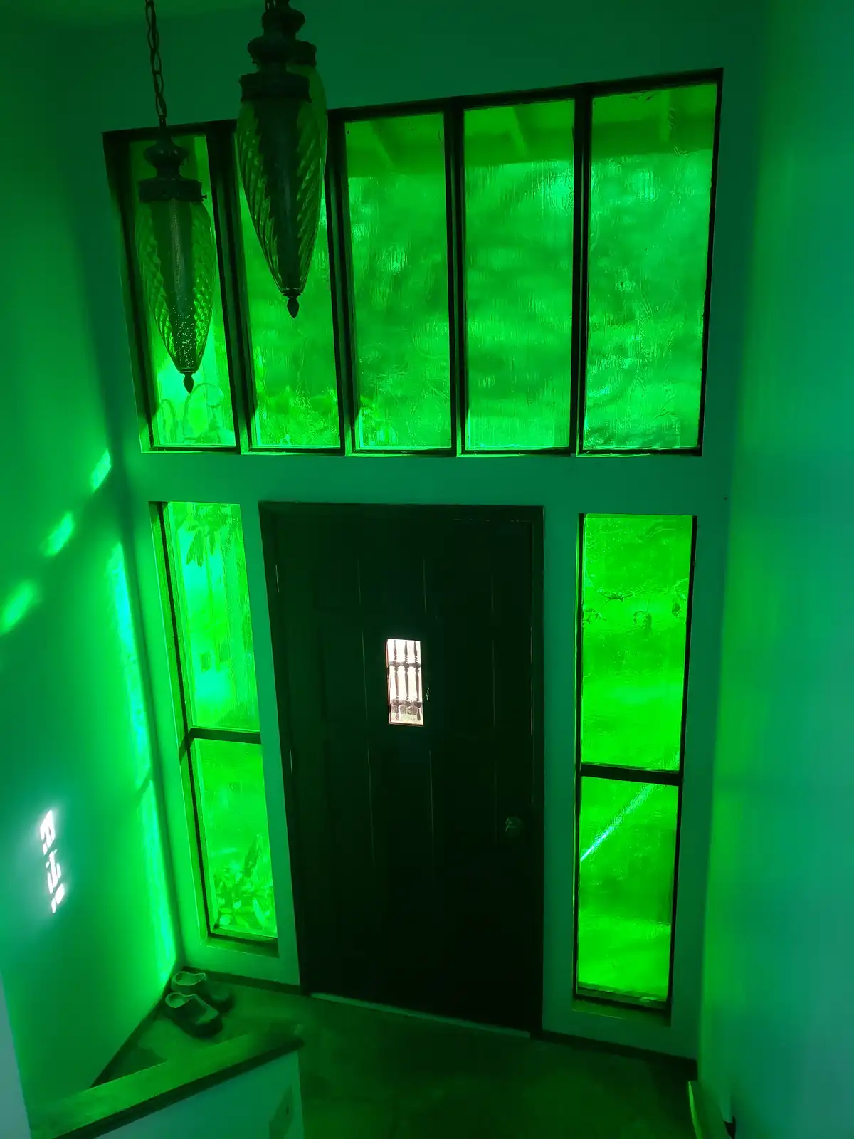 A dimly lit entryway is bathed in an intense, unnatural green glow emanating from frosted glass windows and a hanging lamp…