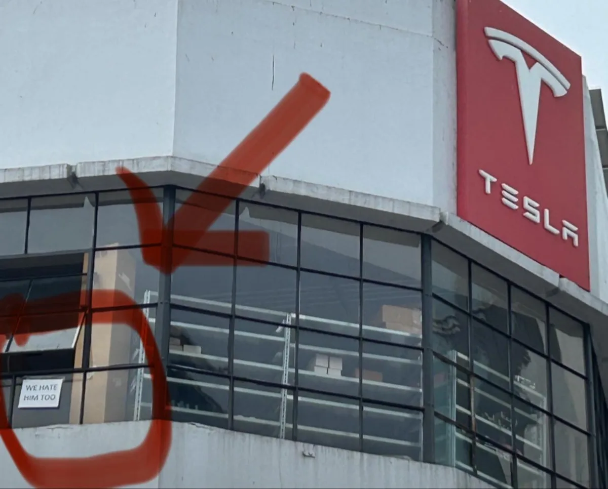 An exterior shot of a Tesla building with its red logo visible. A large red arrow and circle have been digitally added to…