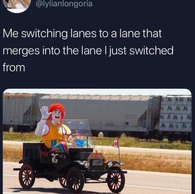 A person in a Ronald McDonald costume drives a vintage black car with red wheels on a highway, waving at the camera. Behind…