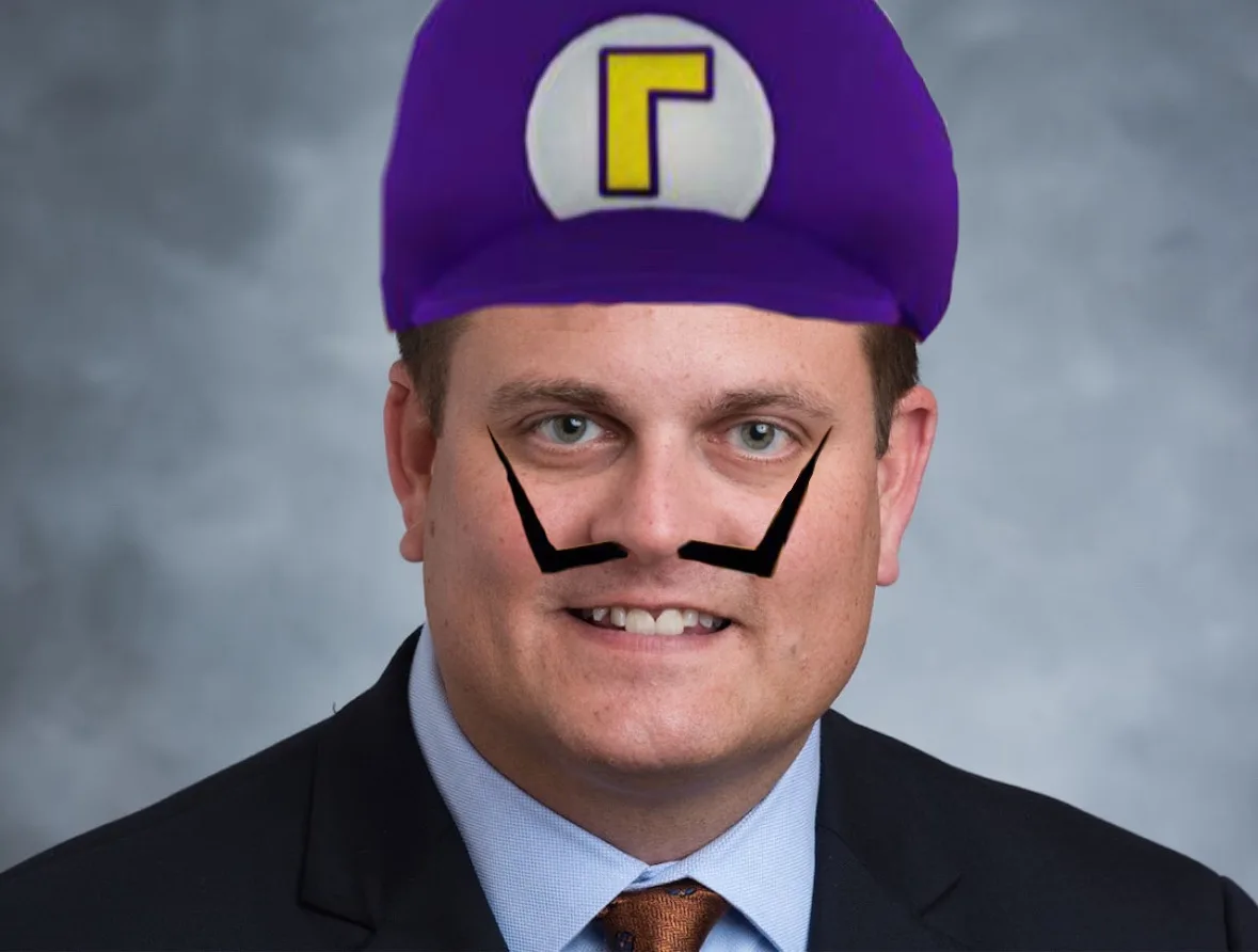A man in a suit and tie has a purple cap with a yellow 'R' logo and a digitally added black mustache drawn on his face…