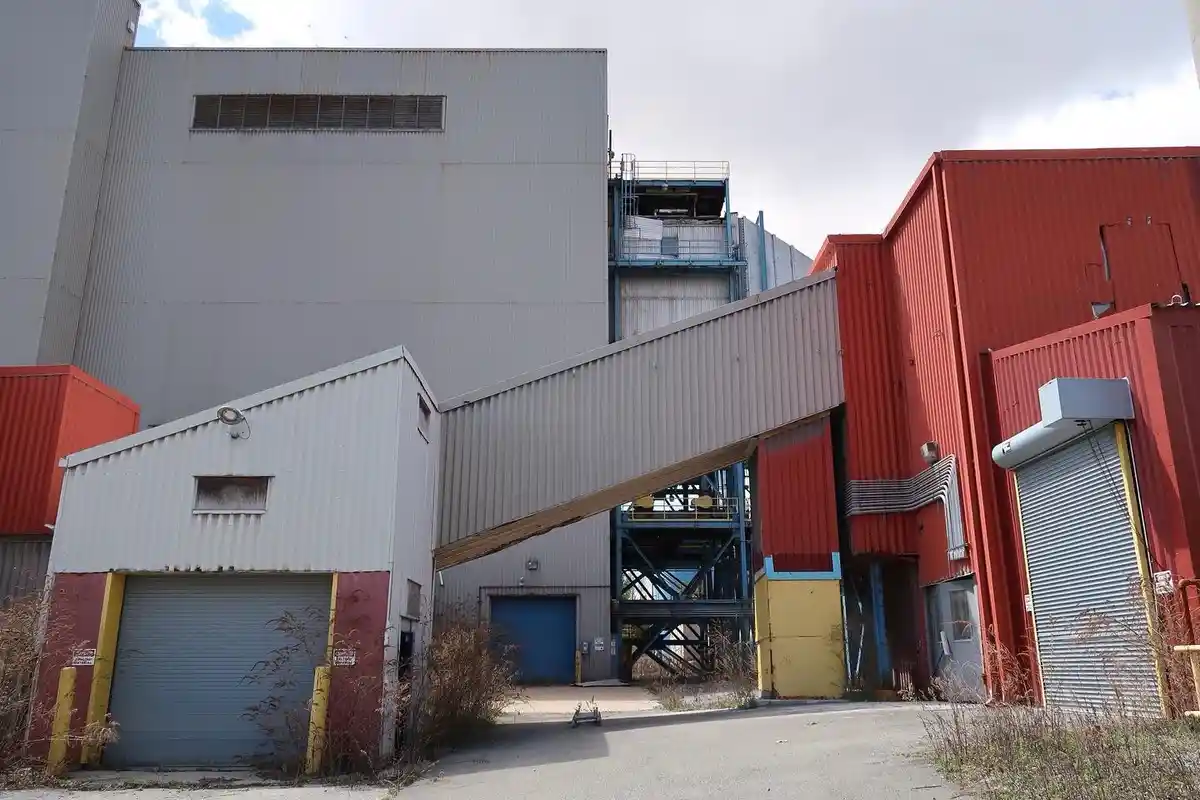 An industrial complex with corrugated metal buildings in red, gray, and white, featuring roll-up doors, a pedestrian bridge…