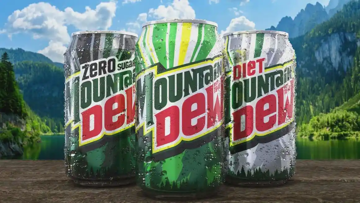 Three chilled Mountain Dew cans—labeled 'Zero Sugar', 'Original', and 'Diet'—sitting on a wooden surface against a scenic…