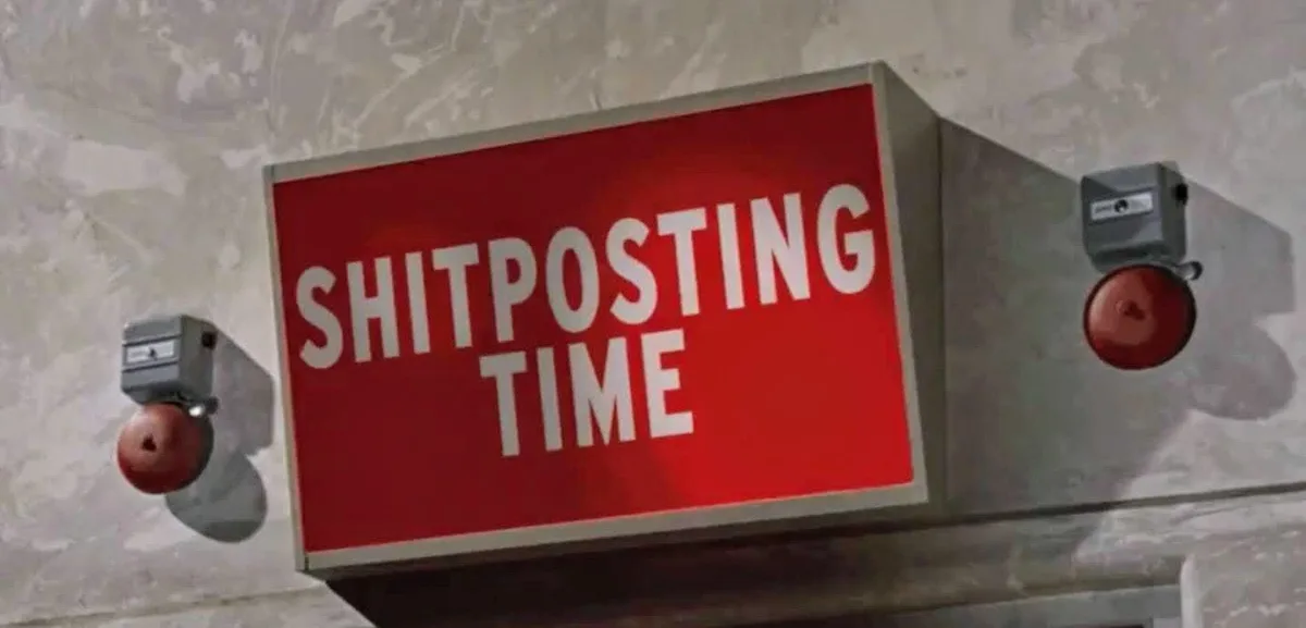 A red sign with white text reading 'SHITPOSTING TIME' is mounted on a concrete wall, flanked by two red emergency alarm…