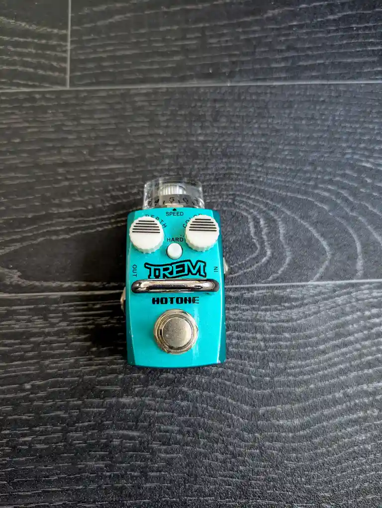 A turquoise Hotone Trem guitar effects pedal with two white knobs labeled 'DEPTH' and 'SPEED', a central footswitch, and a…