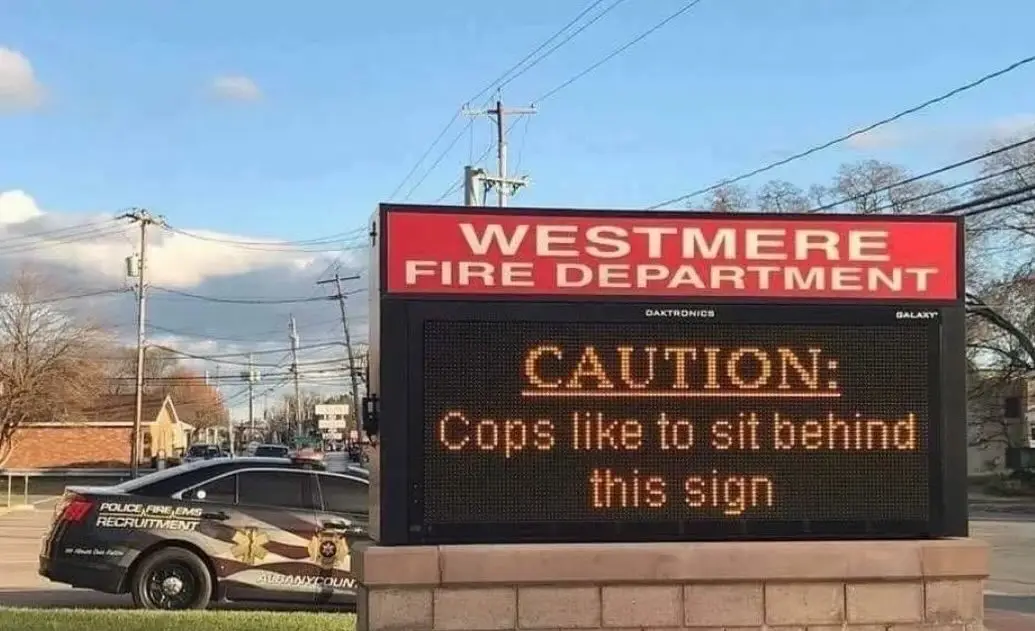 An electronic sign for the Westmere Fire Department displays the message 'CAUTION: Cops like to sit behind this sign' while…