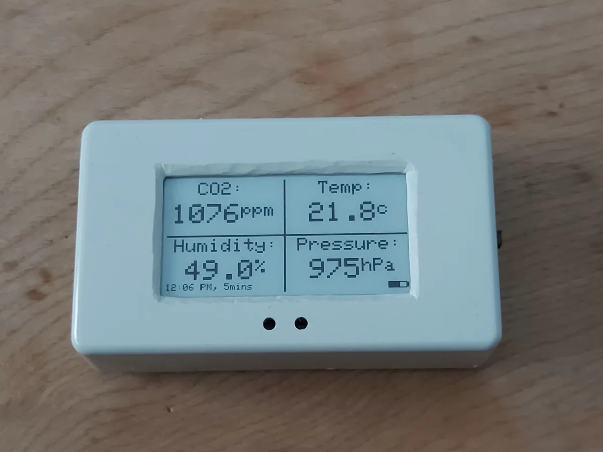 A white rectangular electronic device with a taped-on LCD screen displays environmental data: CO2 at 1076ppm, temperature at…