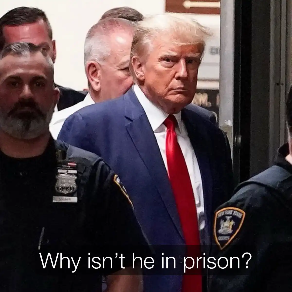 A photo shows Donald Trump in a blue suit and red tie, flanked by New York State Court officers, looking serious as he walks…