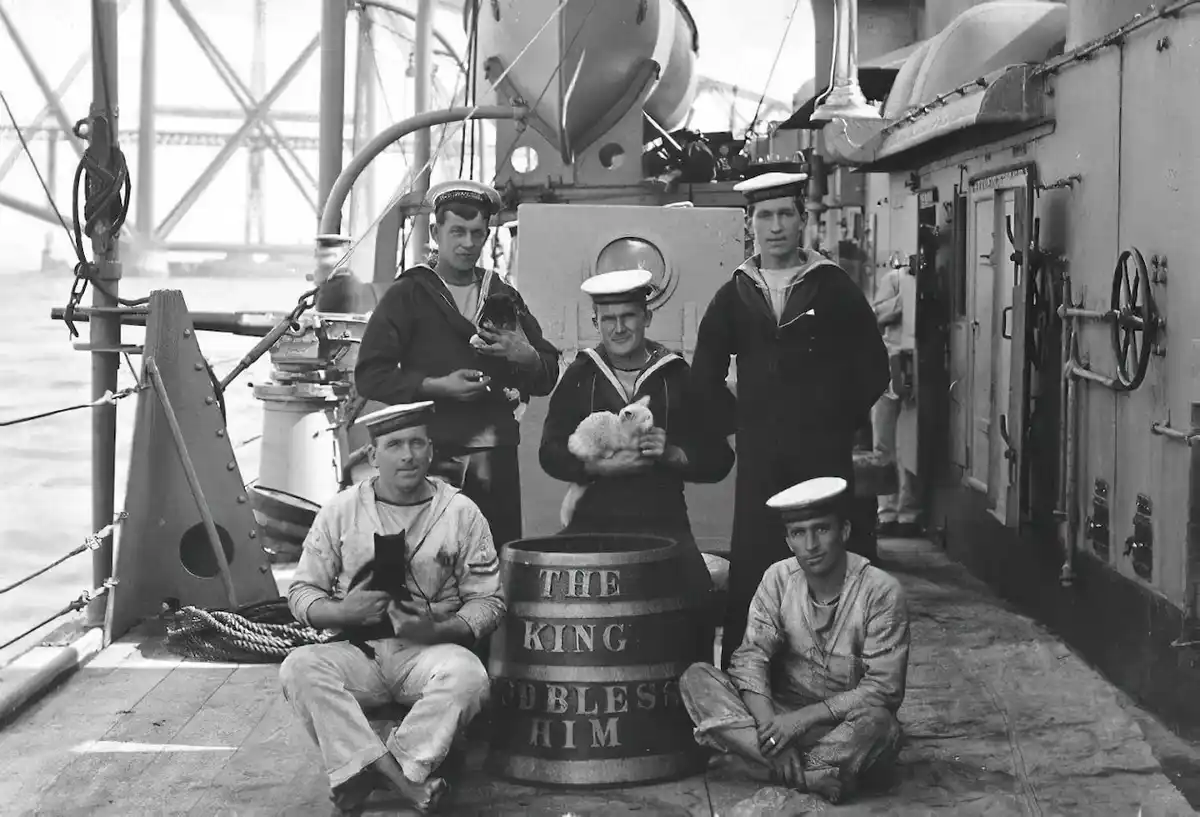 A vintage black-and-white photo shows five sailors posing on a ship's deck, with one holding a small white cat and another…
