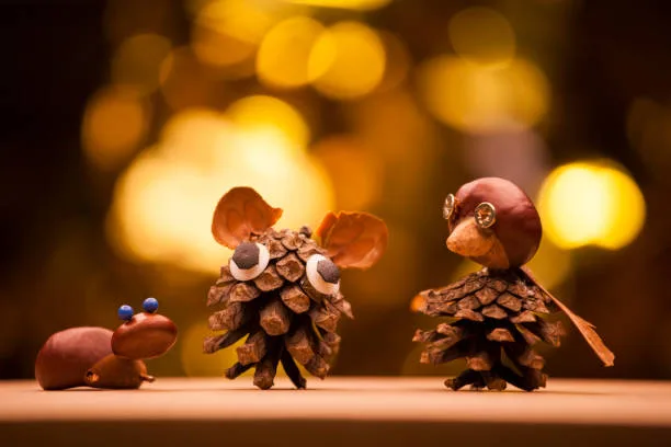 Three whimsical pinecone creatures with googly eyes and acorn hats stand on a wooden surface against a warm, blurred golden…