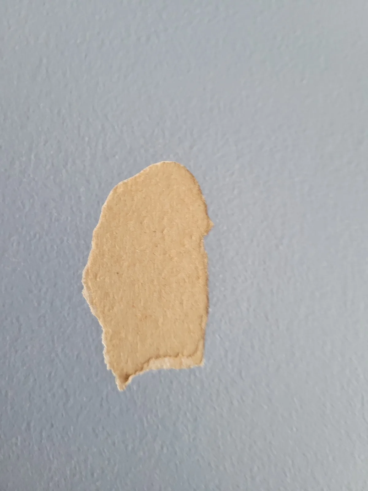 A small, irregularly torn piece of beige paper lies on a textured light blue wall. The overlaid text reads 'i'm not a ghost…