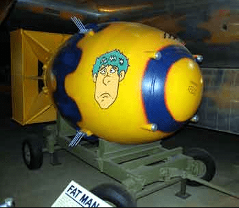 A yellow and blue nuclear bomb, nicknamed 'Fat Man', is displayed on a wheeled cart in a museum. It features a cartoonish…