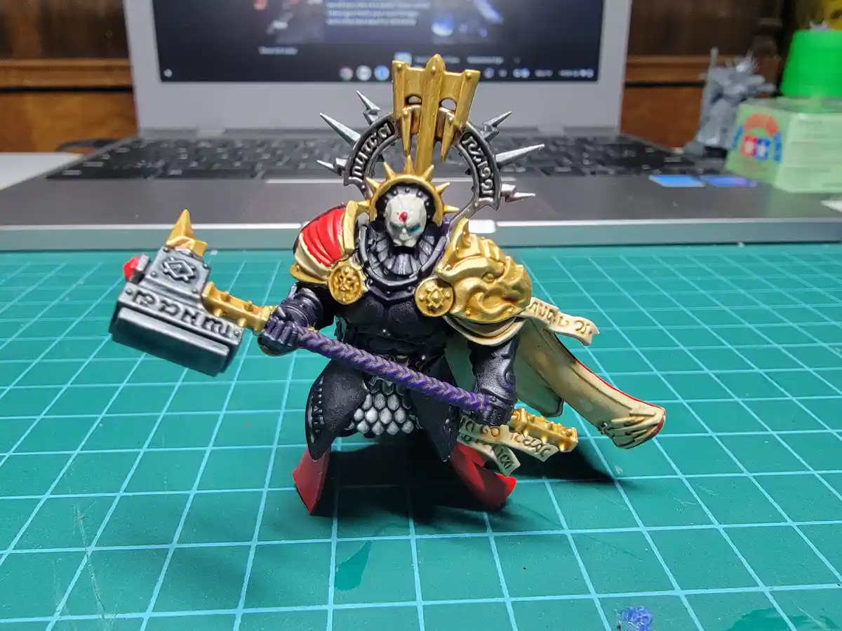 A heavily detailed, painted miniature figure of a fantasy warrior with a skull face, gold and black armor, and a large…