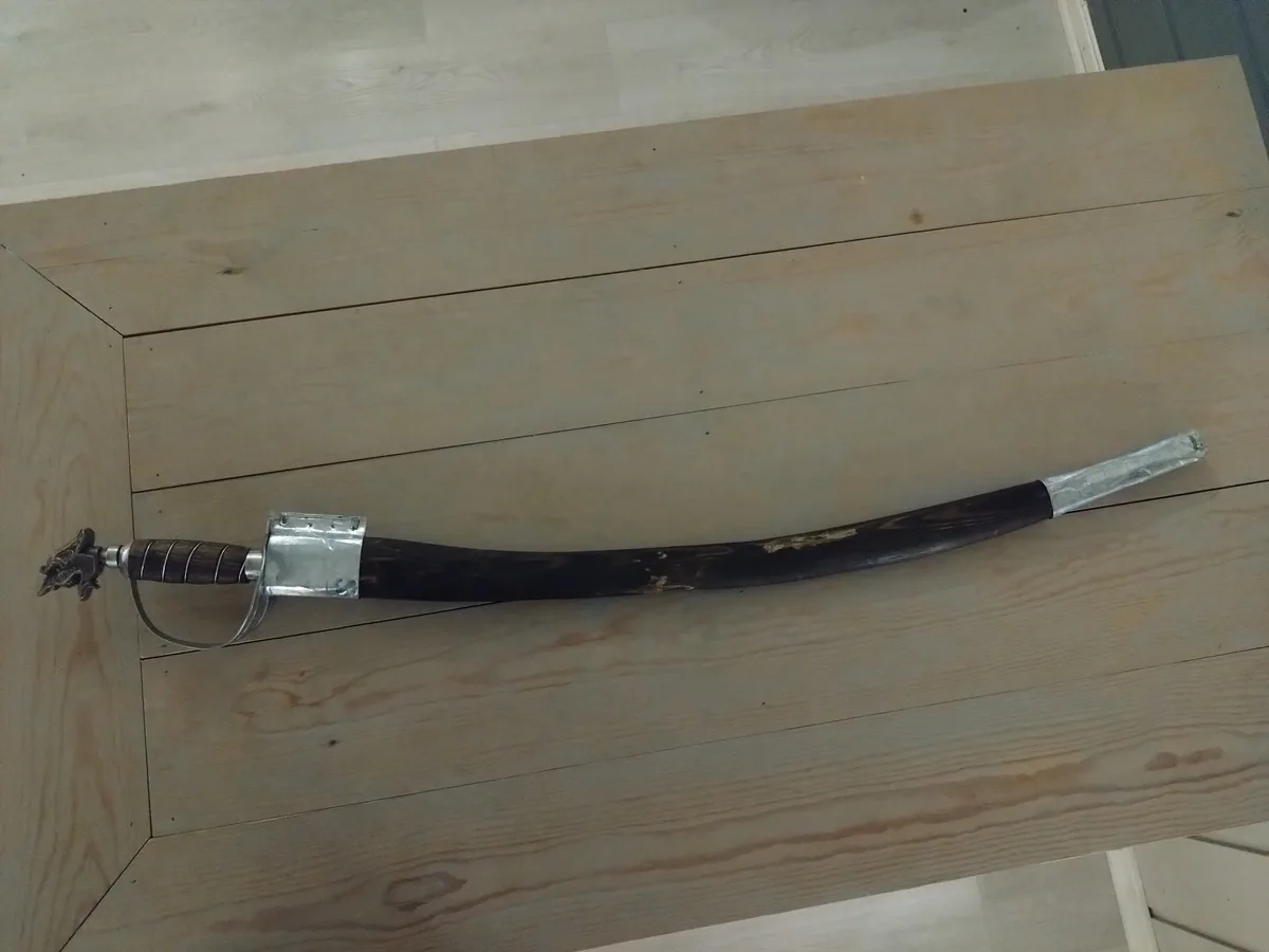A sword with a dark, curved horn blade and a metal hilt lies on a light wooden surface. The overlaid text reads 'my sword is…